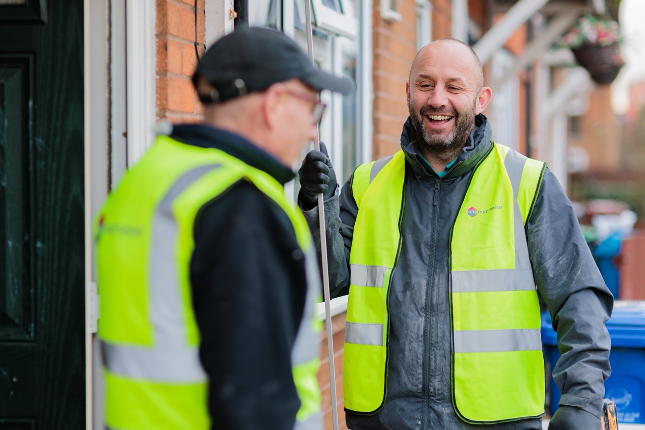 Two men wearing high visibility jackets sat stood outside a property in Manchester having a conversation.