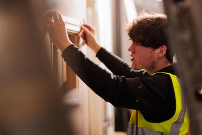 A man working on making an adaptation to a house, hanging a piece of joinery to a wall.