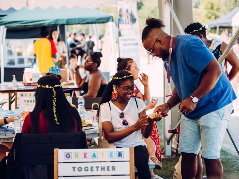 A man helping a little girl at a craft stall at a festival.