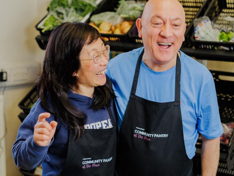 Two people standing close together in front of fruit and veg