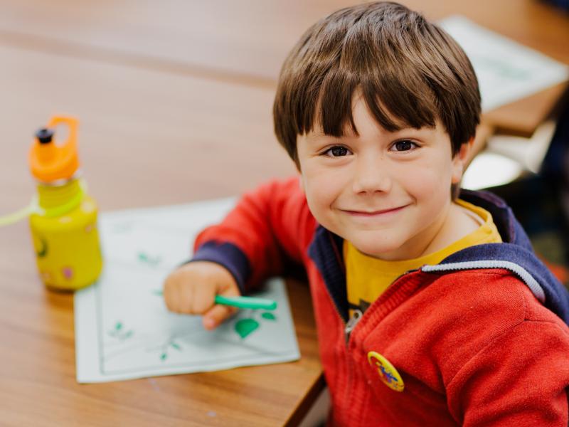 A small child wearing a red jumper, facing the camera and smiling.