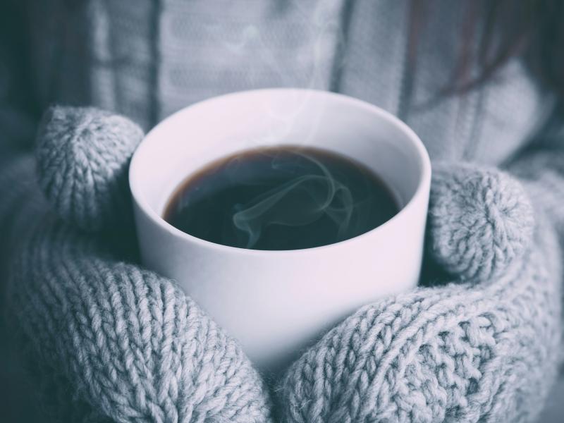 Close up of a person wearing mittens holding a cup