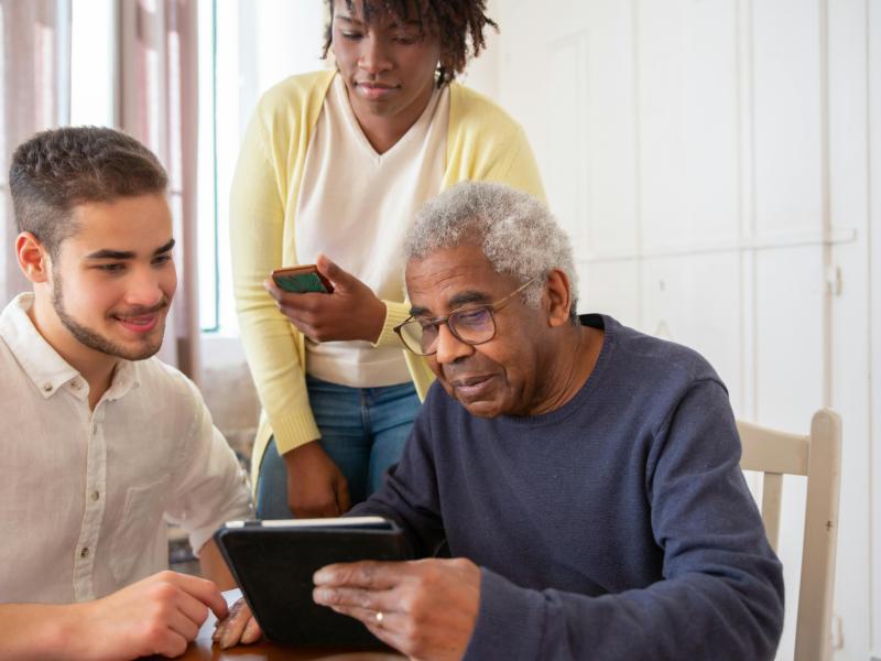 Two people helping a person with a tablet