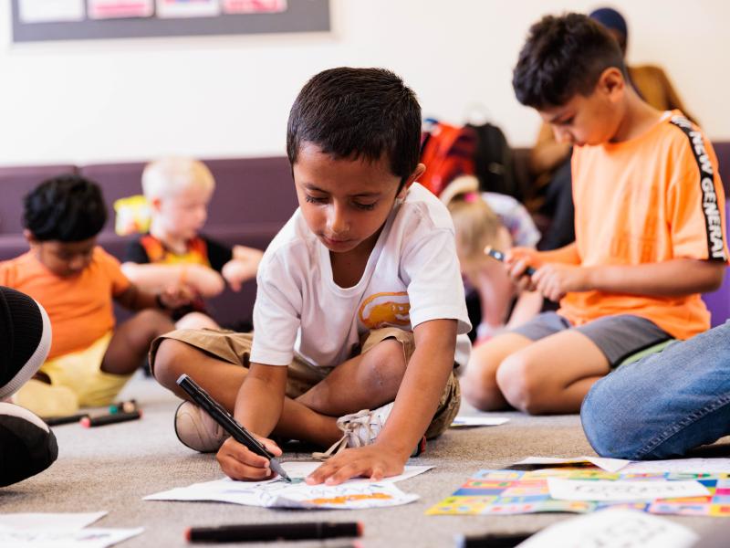 An image of a small boy colouring in a class full of children doing drawing activities