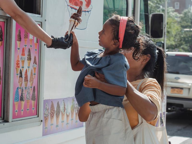 An image of a mother lifting up her daughter to accept an ice cream cone from an ice cream van