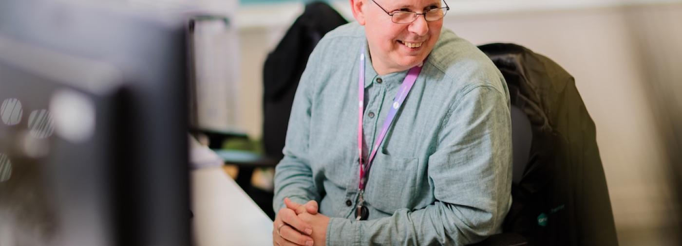 A colleague of One Manchester sat at their desk in conversation with another person.