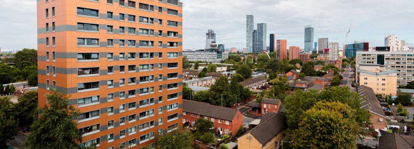 Hopton Court, a building in Manchester. It has orange cladding and the skyline of Manchester can be seen in the background.