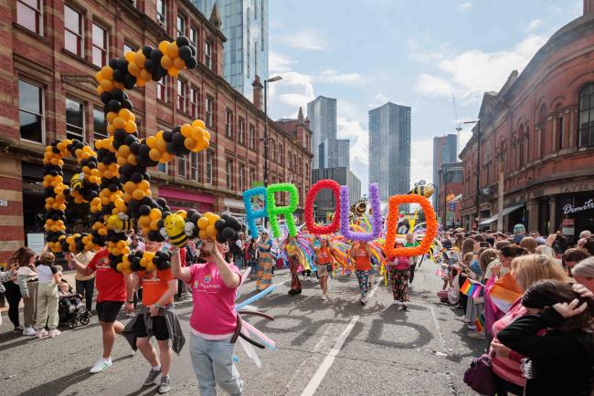 An image of One Manchester Colleagues marching in the Manchester Pride Parade holding balloons that say 'Bee Proud'