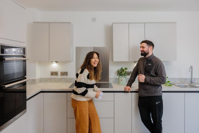 Woman laughing whilst chatting to man in a kitchen over a cup of tea